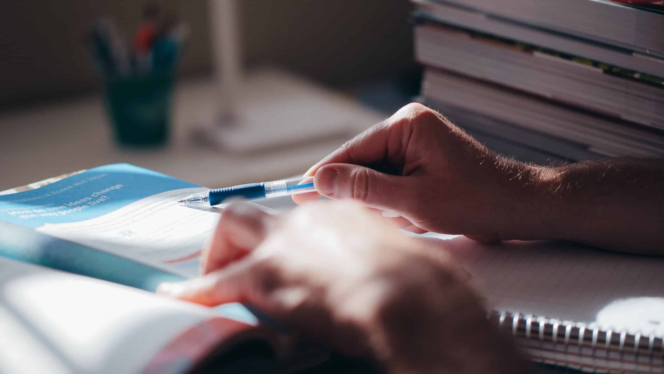 Close-up of hands writing in a notebook with a pen on a desk, suggesting focus and learning.